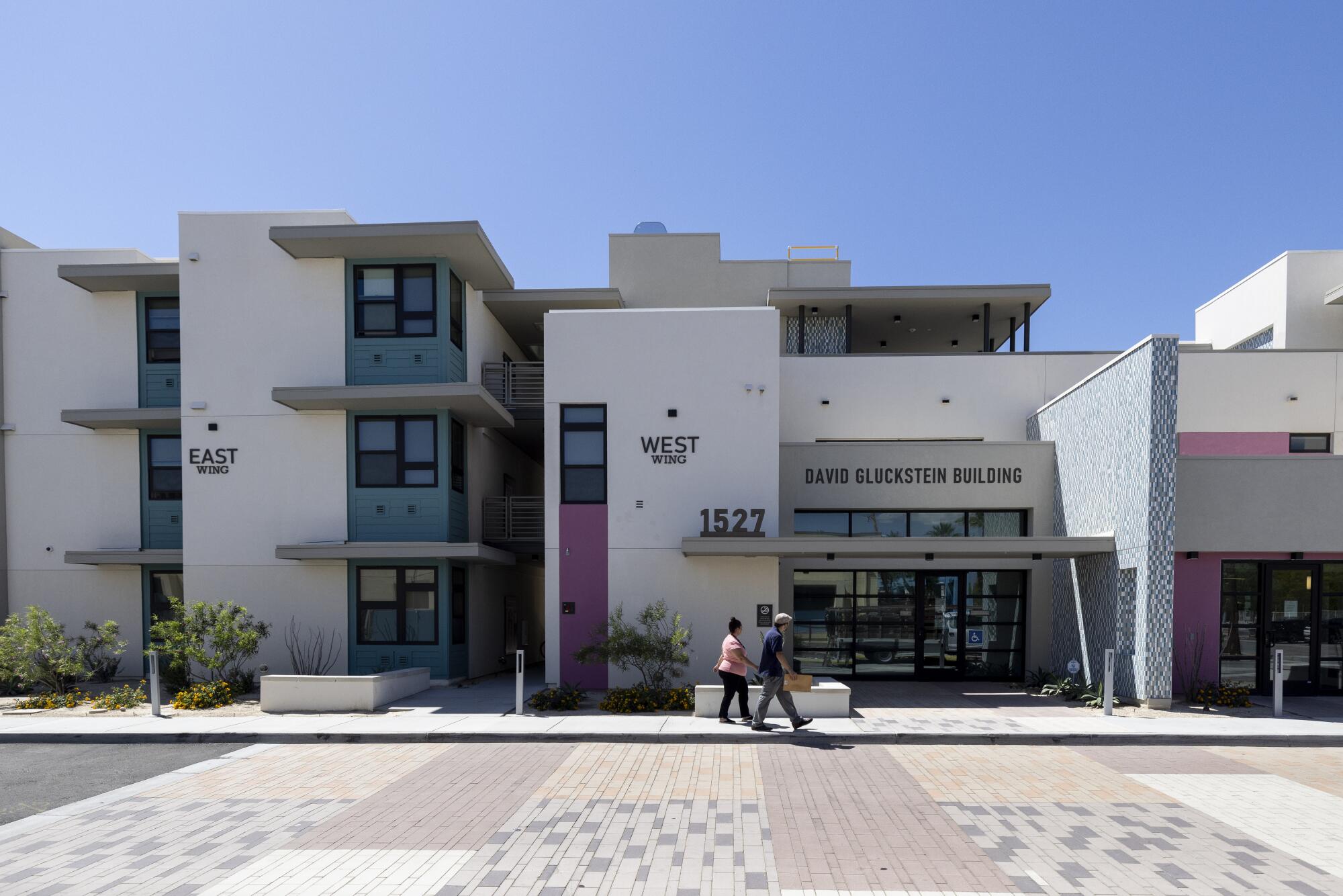 People walk in front of a modern, white housing complex in Palm Springs.