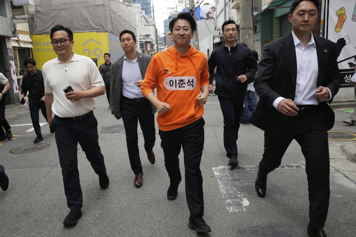 Lee Jun-seok jogs in the street flanked by several men.