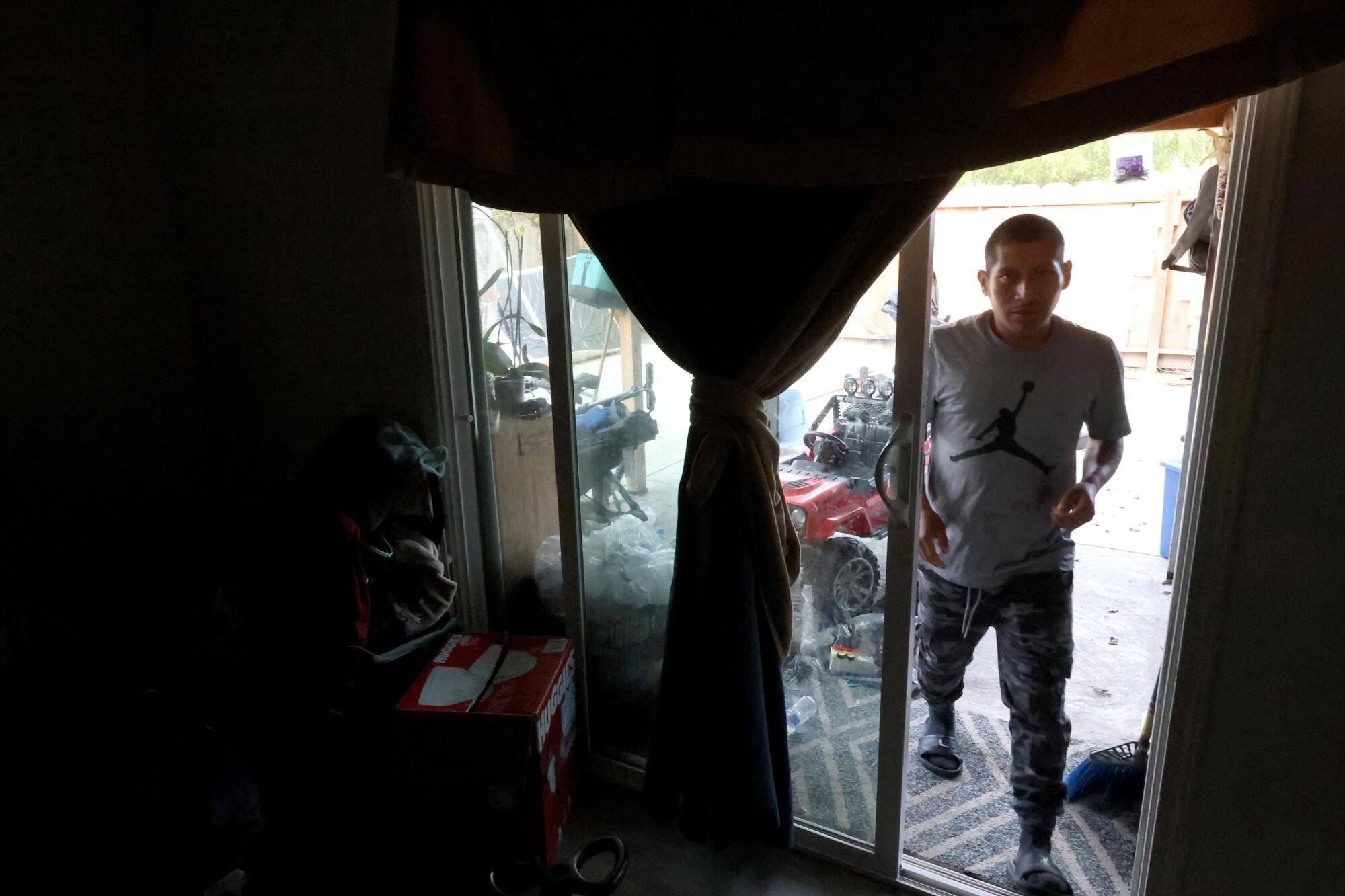 A man enters a darkened home through a sliding glass door.