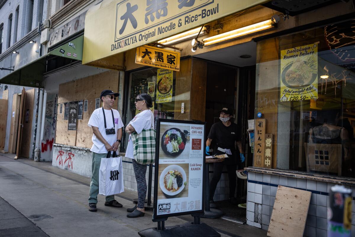 Two people stand outside a boarded up restaurant while a worker opens the door