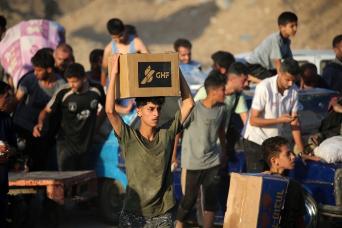 People carrying aid parcels walk along the Salah al-Din road near the Nuseirat refugee camp in the northern Gaza Strip
