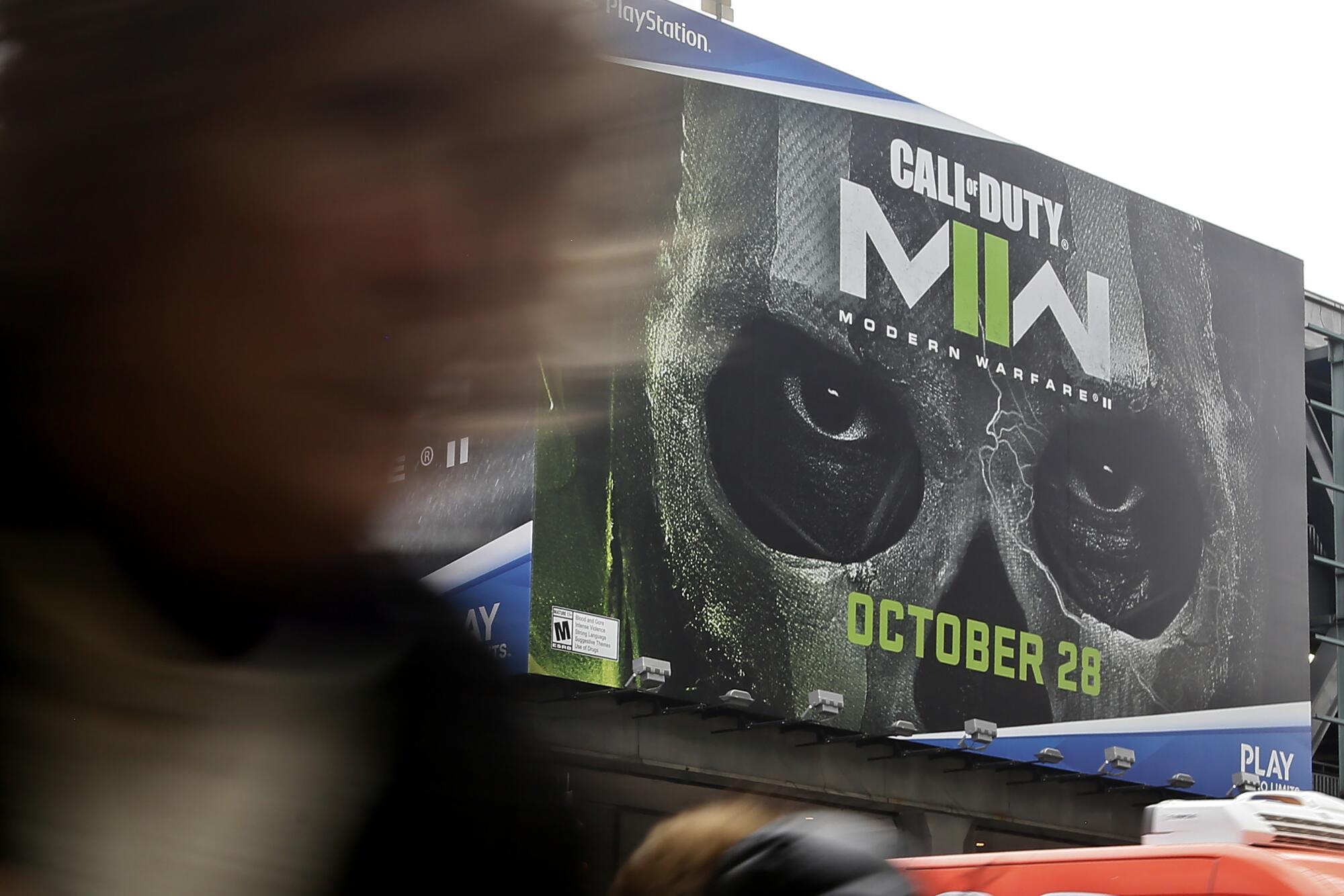 A blurred-out person walking in front of a billboard for "Call of Duty: Modern Warfare II" with someone in a skeleton mask.