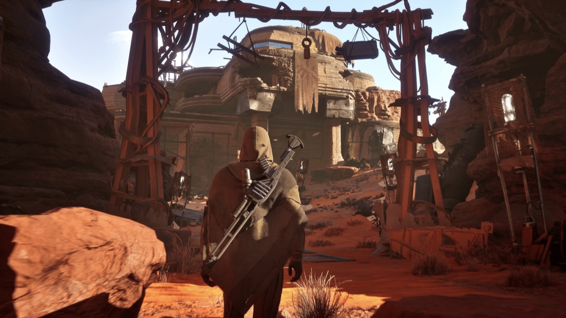 A player walks towards a desert encampment. They are wearing a stillsuit and a hooded cloak
