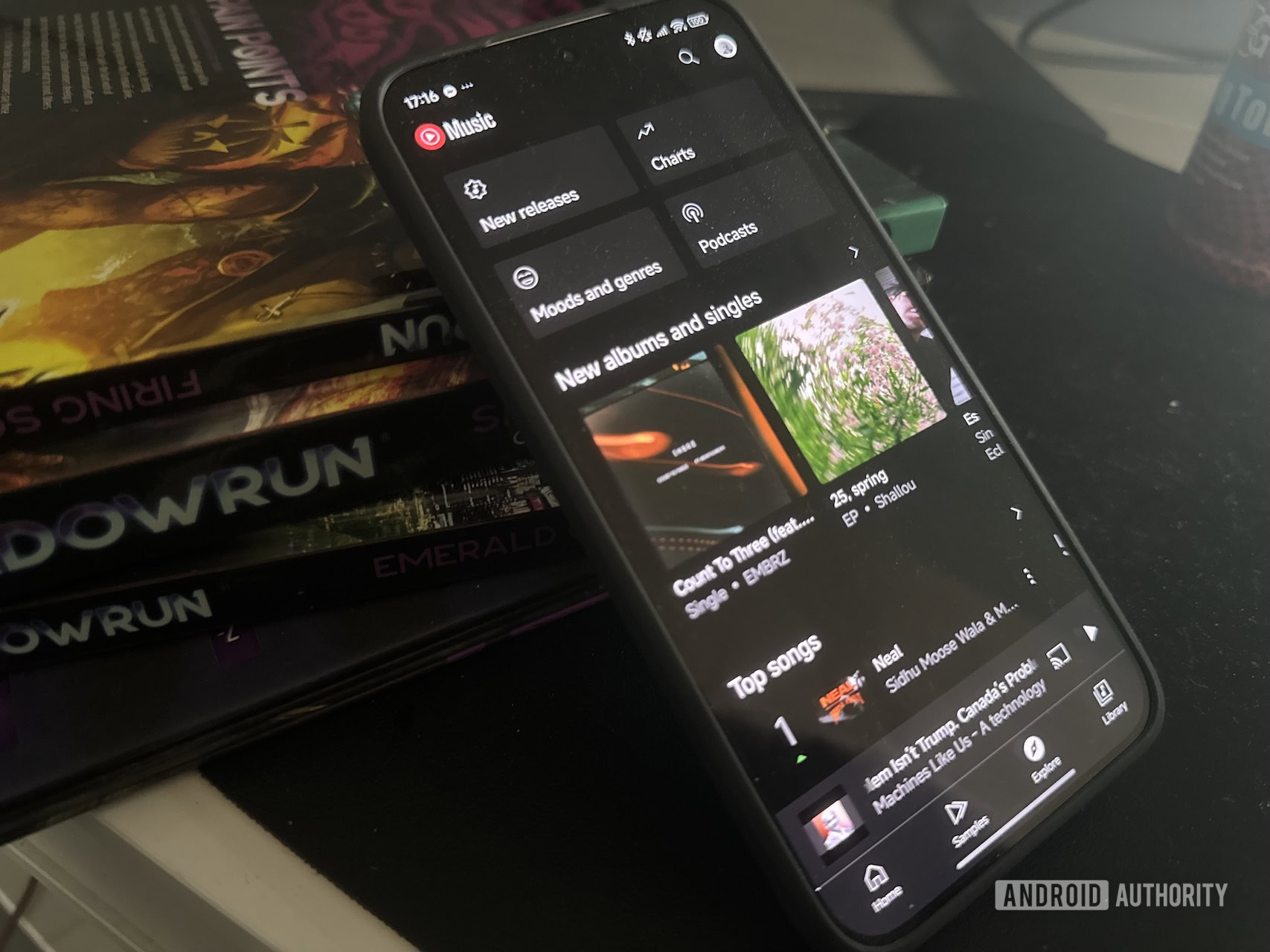 The YouTube Music explore tab on an Android device that is leaning on a stack of black books.