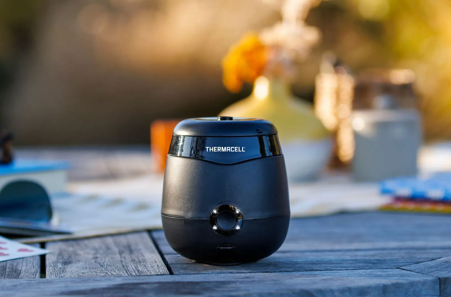 Thermacell mosquito repeller, a small black semi-circular unit, sitting on a picnic table.