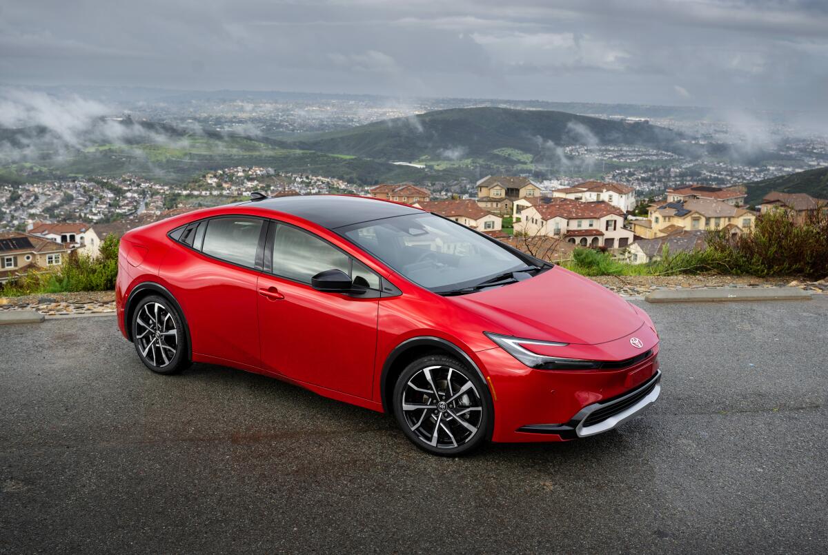 A bright red car parked on a road overlooking homes and hills
