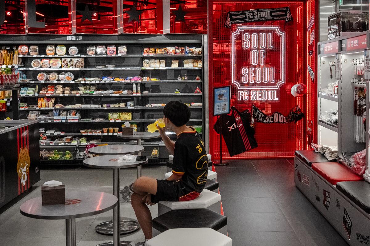 A teenage boy drinks a beverage in the dining area at a GS25 convenience store.