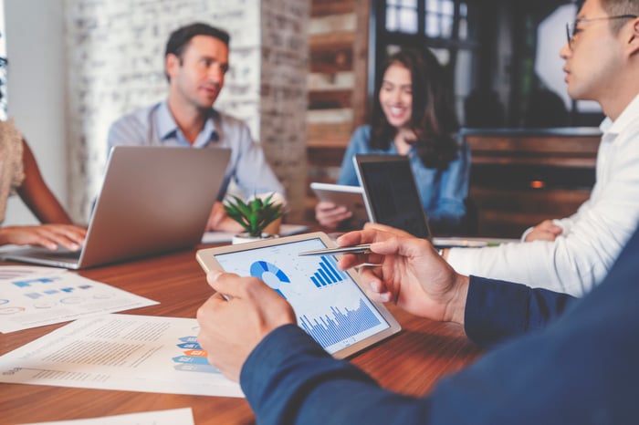 Employees using laptops and tablets to analyze business metrics in a conference room.